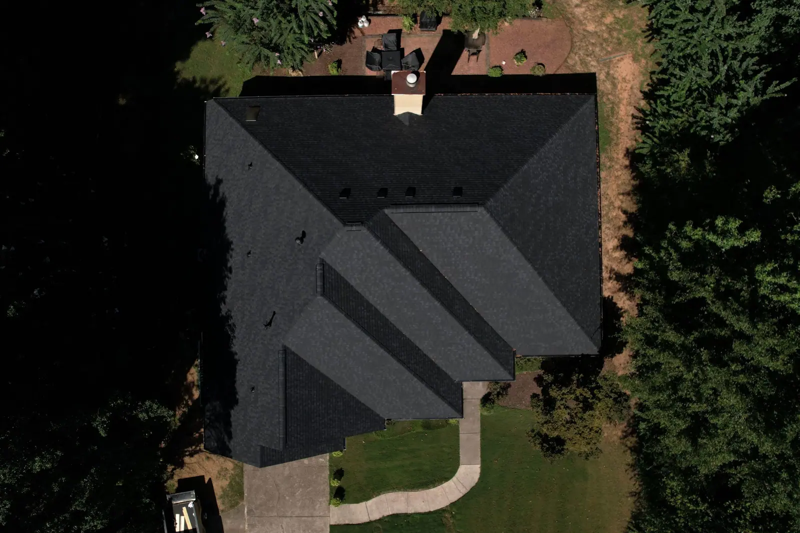 Photo of a new black shingle roof on a home surrounded by woods, finished by Dryco Roofing