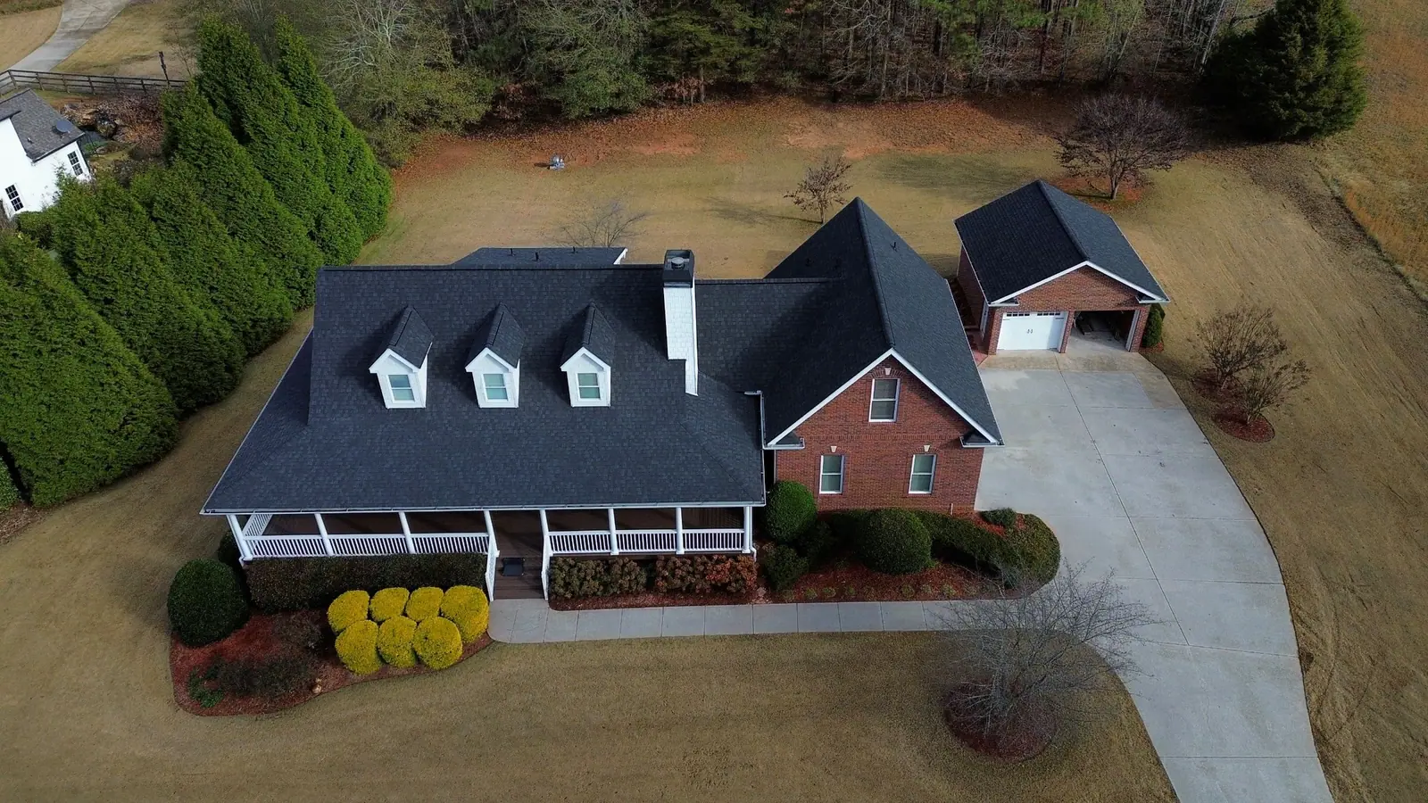 Aerial view of a brick and white farmhouse with three dormers and a new charcoal shingle roof by Dryco Roofing