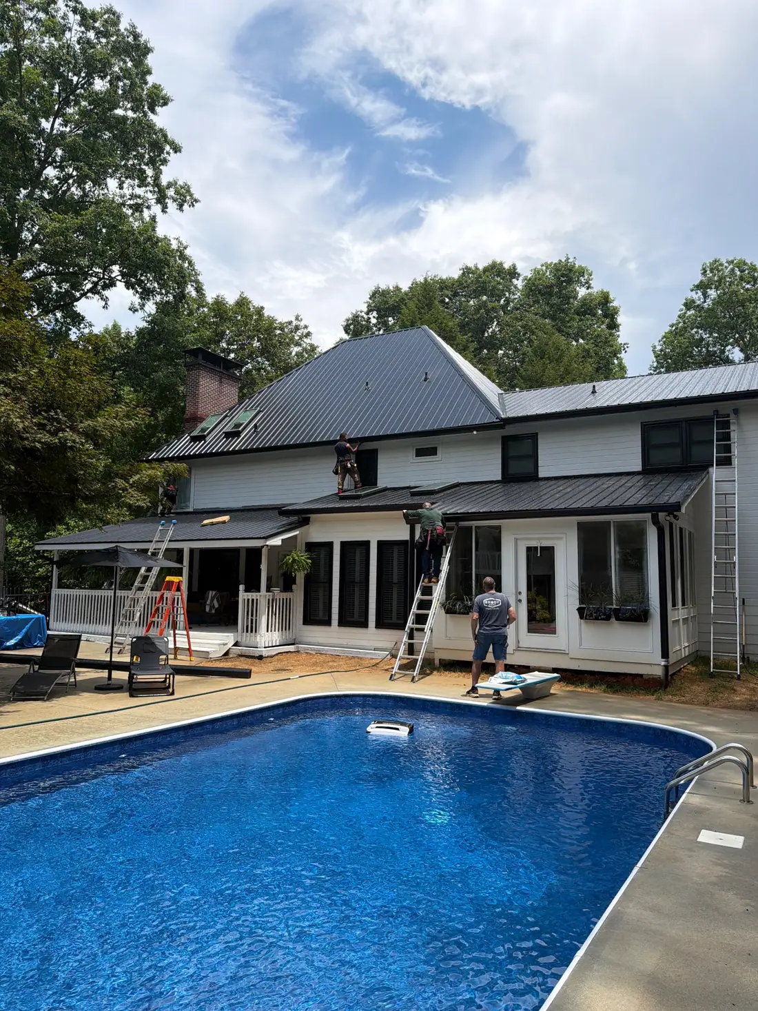 Dryco Roofing crew installing a dark standing-seam metal roof on a white home beside a pool