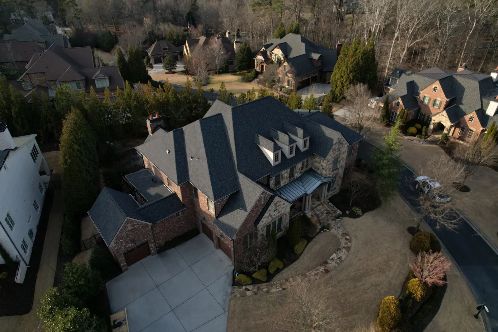 Aerial view of a stone and brick home with a new grey shingle roof and dormers by Dryco Roofing